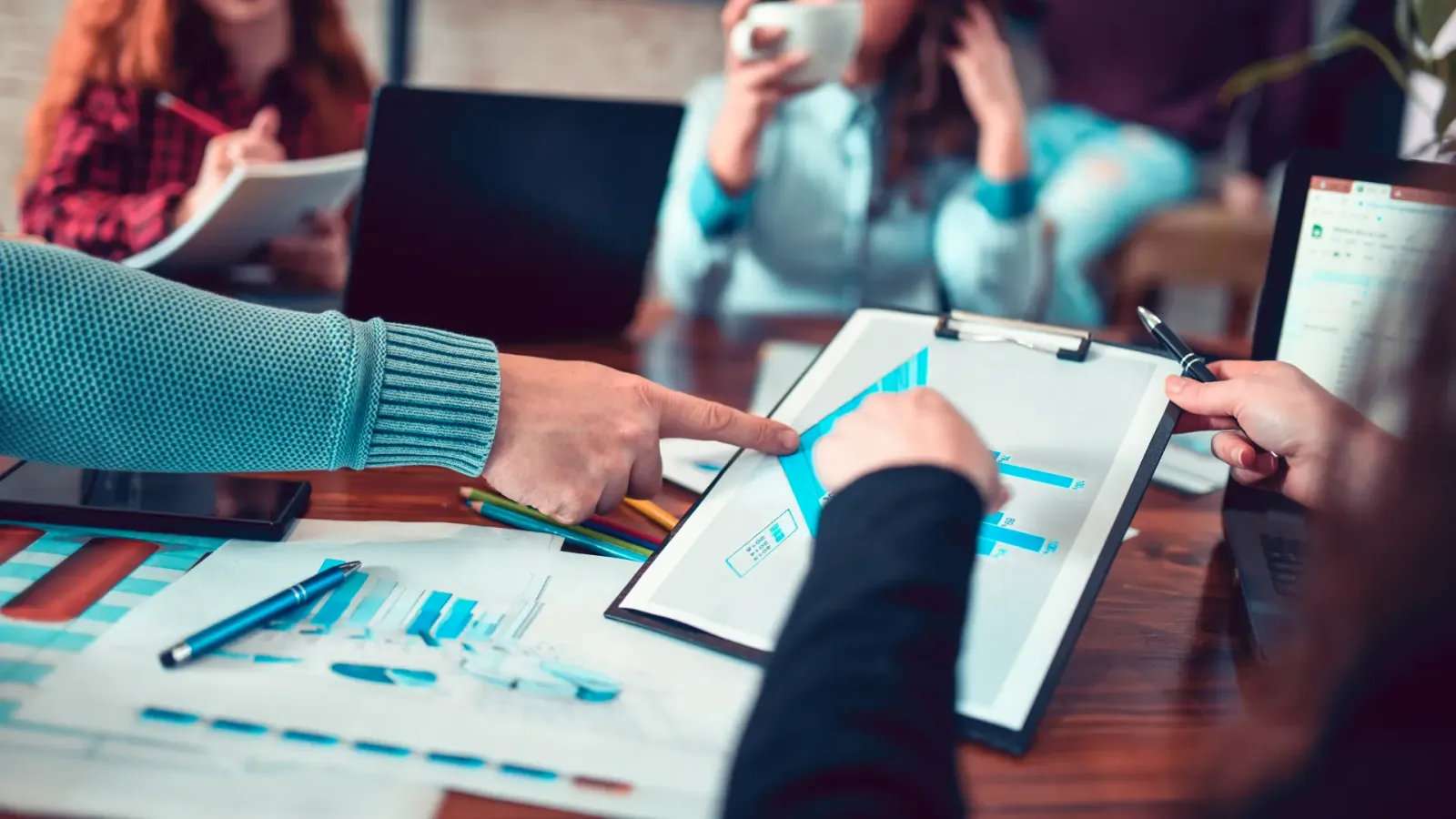 Colleagues pointing at bar charts on a clipboard and on printed reports during a meeting