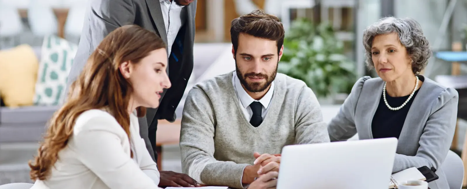 Four colleagues reviewing options together on a laptop in a bright office